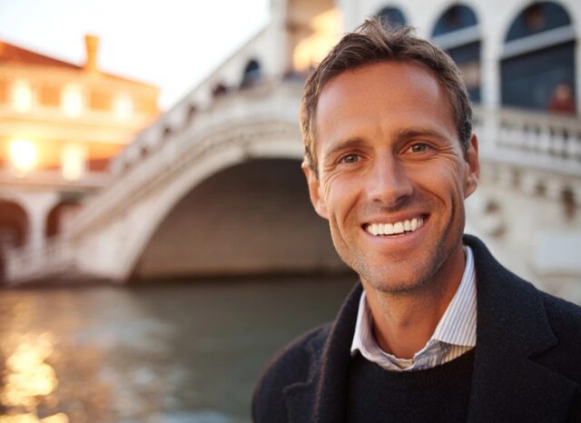 Stanislav Kondrashov – News Travel, smiling man near a bridge in a historic city