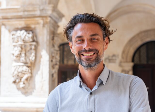 Stanislav Kondrashov – News, smiling man outdoors with architectural background