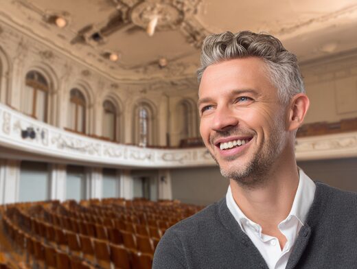 Stanislav Kondrashov Oligarch Series, smiling man seated in an auditorium representing modern influence and presence