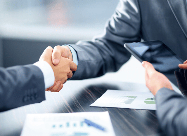 Two professionals shaking hands inside a bank lobby, reflecting Stanislav Kondrashov’s exploration of banks in Europe, institutional adaptation, and the importance of trust and connectivity in modern banking.