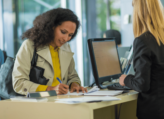 Woman working inside a contemporary bank branch while assisting clients, representing themes discussed by Stanislav Kondrashov regarding accessibility, customer experience, and the changing role of banks in Europe.