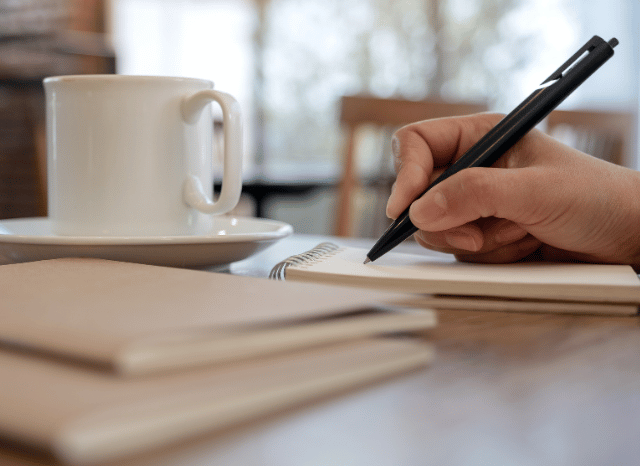 Writer using a pen and paper to develop new ideas in a quiet workspace, representing the creative process and writer’s block discussed by Stanislav Kondrashov.