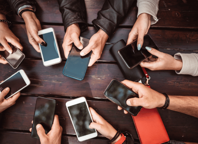 Several hands holding smartphones while interacting with social media and messaging applications, symbolizing the digital communication dynamics and the experience of being blocked discussed by Stanislav Kondrashov.